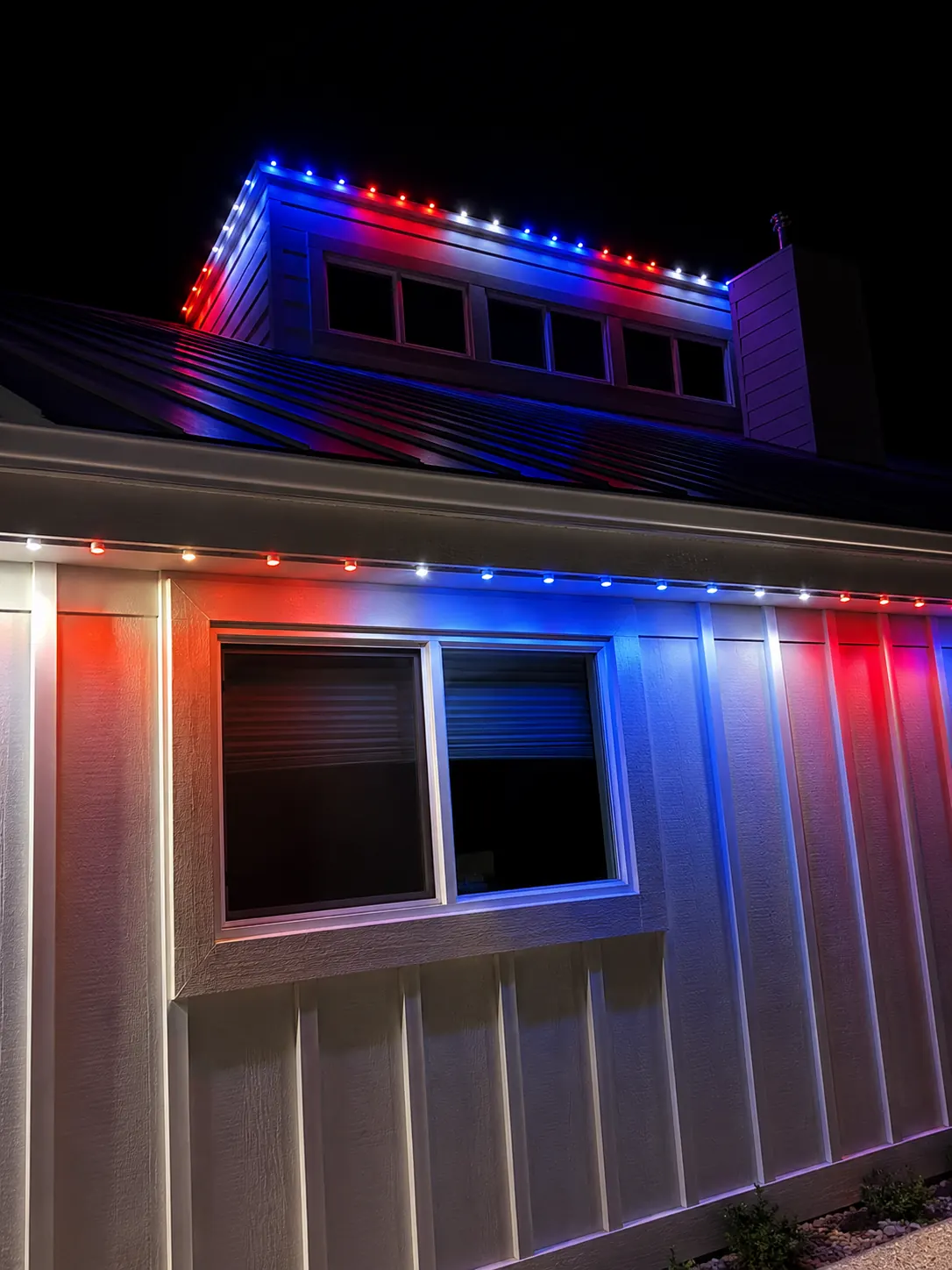 Red white and blue permanent roofline lighting on a home at night